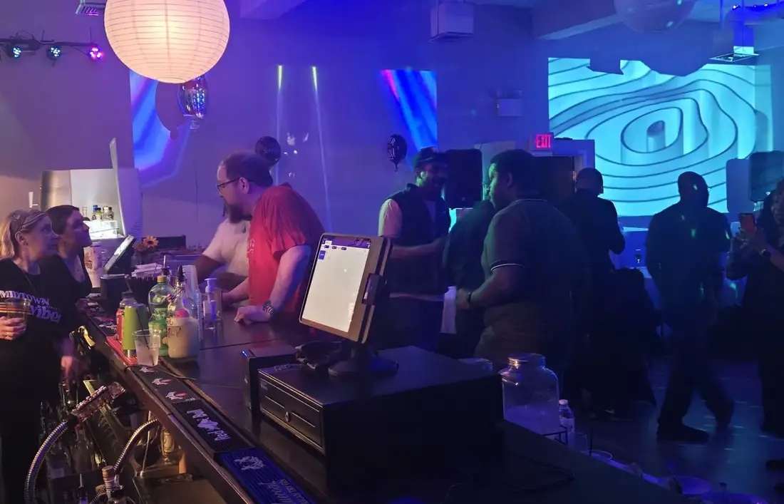 Bartenders serving guests at the upstairs bar in Midtown Hall under blue and purple lighting.