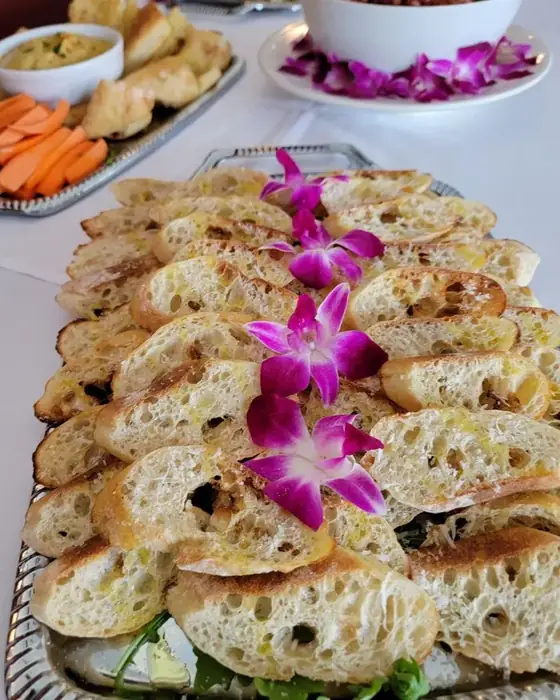 A silver tray of grilled crostini dressed with orchids, with hummus and crudité alongside.