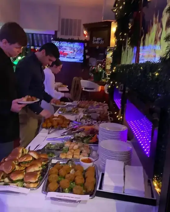 A labeled catering buffet at a corporate holiday party with short rib sliders and vegetarian arancini.