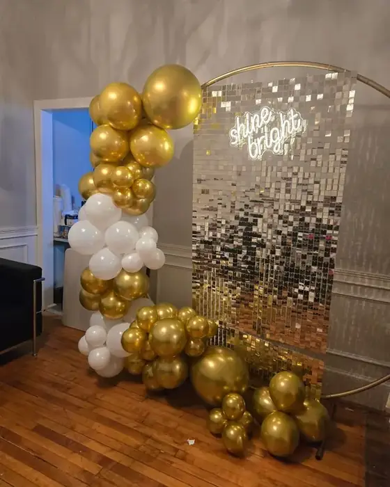 A gold and white balloon arch beside a silver sequin shimmer wall with a neon shine bright sign at Midtown Social.