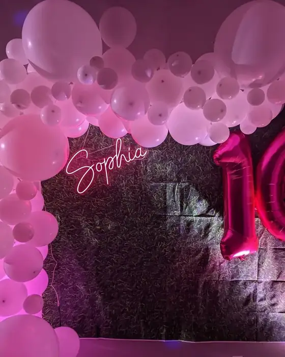 A pink and white balloon arch with a personalised neon name sign and giant number sixteen balloons set up for a sweet sixteen at Midtown Social.