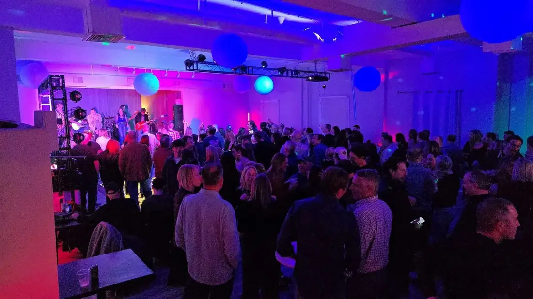 Midtown Hall packed with several hundred guests watching a live band on stage under blue and purple lighting.