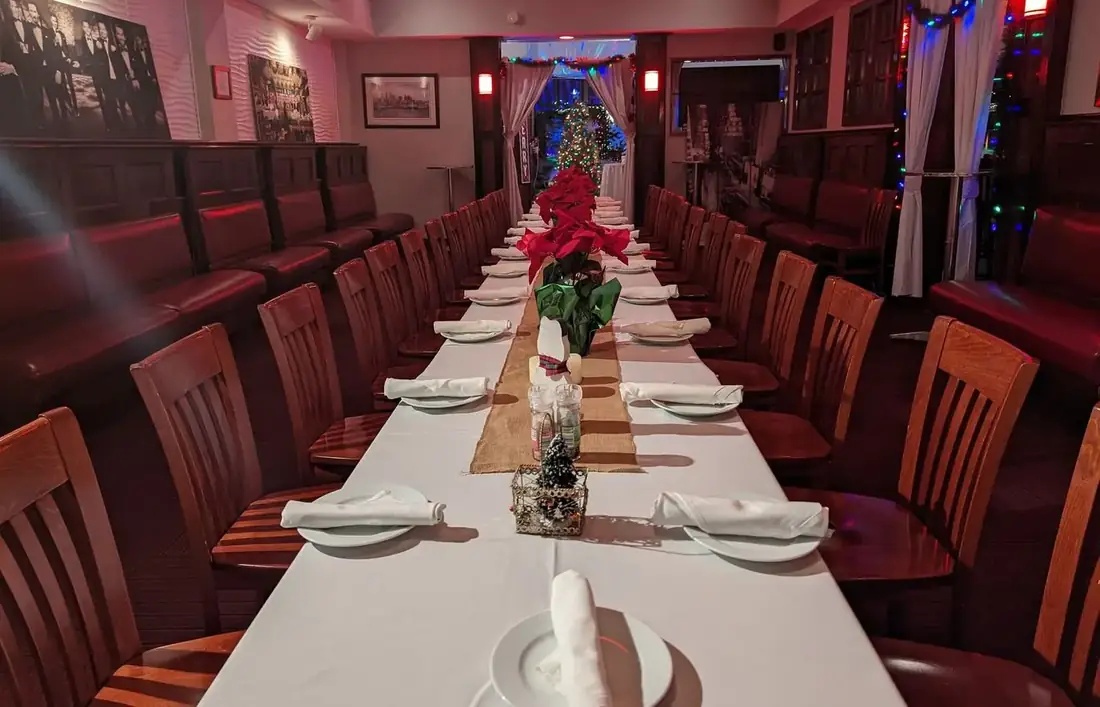 A long table set for a holiday party at Midtown Social with white linen, poinsettias and Christmas lights along the windows.