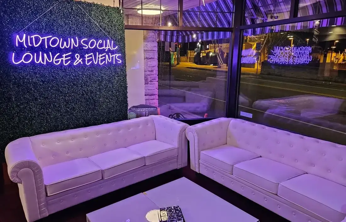 The front lounge at Midtown Social with white tufted sofas beneath the Midtown Social Lounge and Events neon sign, Lancaster Avenue through the windows.
